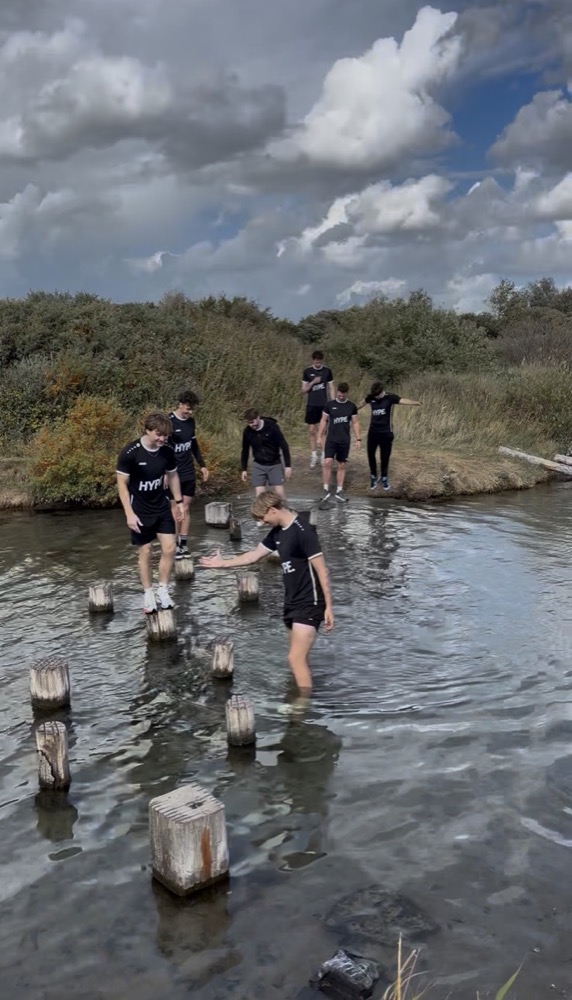 Het team stapt over palen door het water